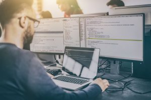 homem em frente a monitores trabalhando com códigos de programação