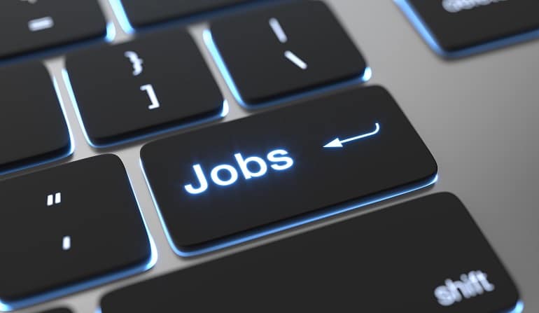 Um teclado de computador é mostrado em close, destacando uma tecla preta iluminada em azul com a palavra “Jobs” escrita no centro. A tecla possui o ícone de uma seta curva, semelhante ao de “Enter”, sugerindo uma função de acesso rápido relacionada a empregos. As outras teclas ao redor aparecem levemente desfocadas. (vagas)
