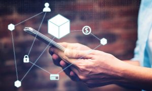 Imagem conceitual de tokenização, mostrando uma mão segurando um cubo digital brilhante no centro, representando tecnologia blockchain. Em torno do cubo, ícones relacionados a finanças, segurança e metas, como cadeado, cifrões e gráficos, conectados por linhas que simbolizam interconexão digital
