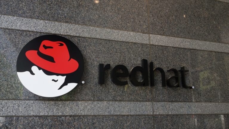 Logotipo da Red Hat em uma parede de granito, com o ícone de um chapéu vermelho em um círculo preto ao lado da palavra 'redhat' em letras minúsculas pretas