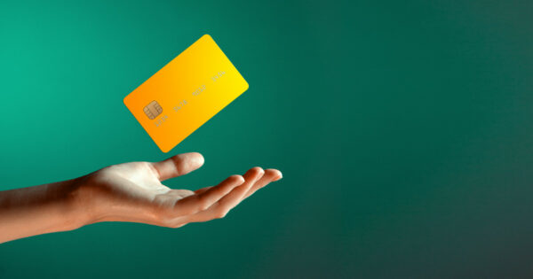 Mão aberta com a palma para cima, segurando um cartão de crédito amarelo flutuando em um fundo verde. A imagem simboliza a facilidade e acessibilidade dos serviços financeiros digitais, crédito social