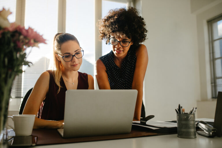 Duas mulheres no escritório conversando e olhando para o notebook.