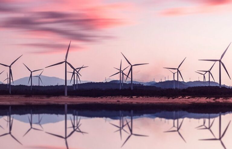 Turbinas eólicas espelhadas na água durante o pôr do sol
