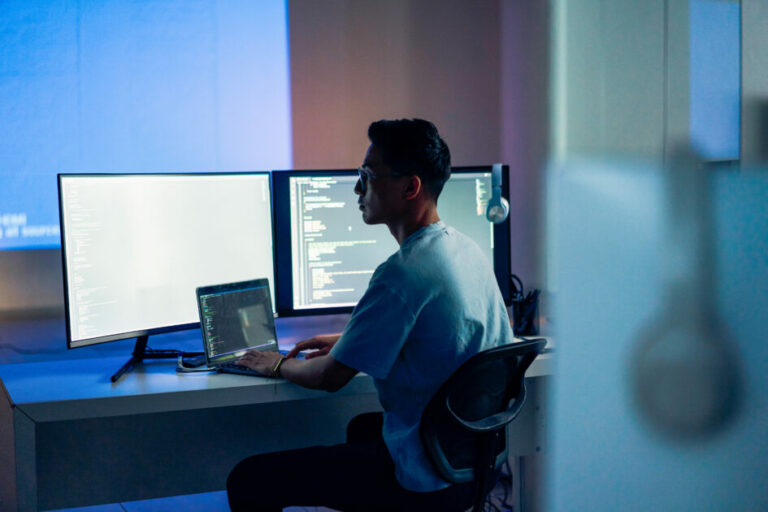 Pessoa programando na frente do computador, em um escritório com pouca iluminação