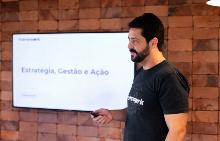 Homem apresentando conteúdo sobre Outsourcing de TI em uma TV. Atrás dele há uma grande parede de tijolos.