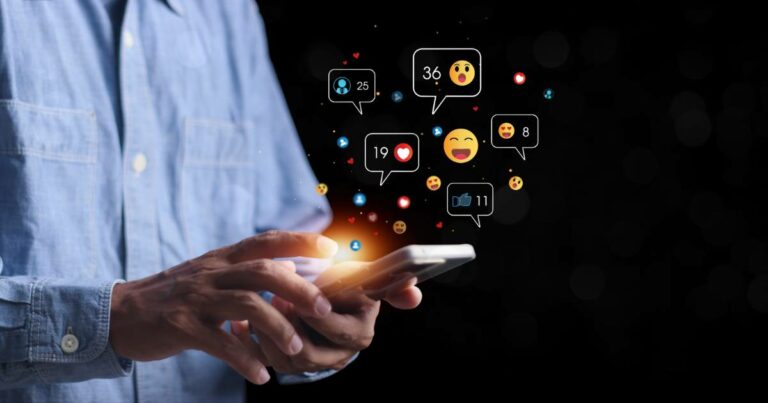 Pessoa utilizando um smartphone enquanto ícones de interações digitais, como curtidas, comentários e reações com emojis, flutuam ao redor da tela. O fundo escuro destaca a luminosidade dos ícones, representando o engajamento em redes sociais e o impacto da tecnologia na comunicação, abx, hiperpersonalização ( IA generativa), ABM, (BRQ), profissionais
