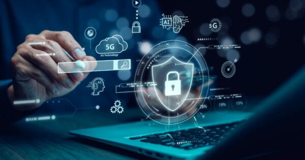 Mão segurando um ícone digital interativo em formato de escudo com cadeado, representando segurança digital, sobre um laptop. O fundo contém elementos tecnológicos como ícones de 5G, nuvem, inteligência artificial e gráficos, simbolizando conectividade, inovação e proteção de dados. (ANPD, TLS negócio, negócios)