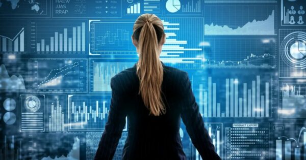 A imagem mostra uma mulher de costas, vestindo um terno escuro, observando uma tela digital repleta de gráficos, estatísticas e dados analíticos em tons de azul. A cena transmite um conceito de análise de dados, inteligência artificial e tomada de decisões baseadas em informações digitais. (dados, analytics, data driven, afip, gartner)