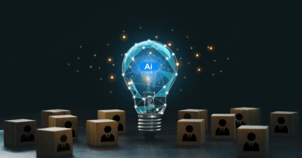 Imagem de uma lâmpada transparente iluminada, com um circuito digital e a sigla "AI" (inteligência artificial) no centro, representando inovação tecnológica. Ao redor da lâmpada, há blocos de madeira com ícones de pessoas em traje social, simbolizando o uso da inteligência artificial em contextos de negócios e gestão de pessoas. O fundo escuro destaca os elementos digitais brilhantes, sugerindo tecnologia e criatividade (médias e grandes empresas, ONGs)