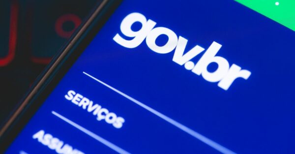 Imagem em close-up do ecrã de um smartphone a exibir a interface do portal digital do governo brasileiro, com o logótipo “gov.br” em letras brancas sobre um fundo azul. Abaixo, vê-se parcialmente a palavra “SERVIÇOS”, sugerindo a navegação por opções disponíveis no site. A imagem transmite a ideia de acesso digital a serviços, segurança, públicos, gargalos