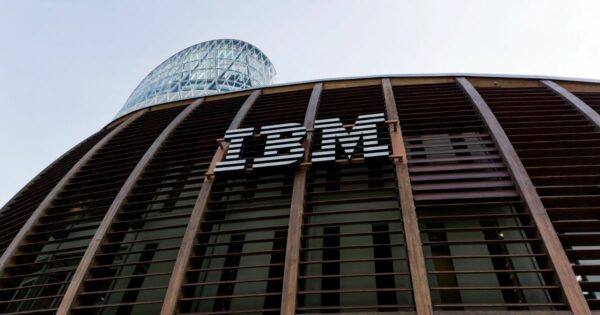 Fachada moderna de um edifício com o logótipo da IBM em destaque, com estrutura em madeira e vidro e uma torre envidraçada ao fundo."