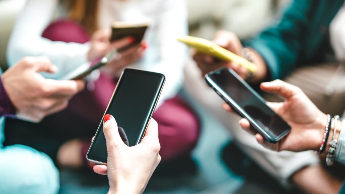 Imagem de várias pessoas usando smartphones ao mesmo tempo, focando nas mãos e dispositivos móveis, em um ambiente social (fraudes)