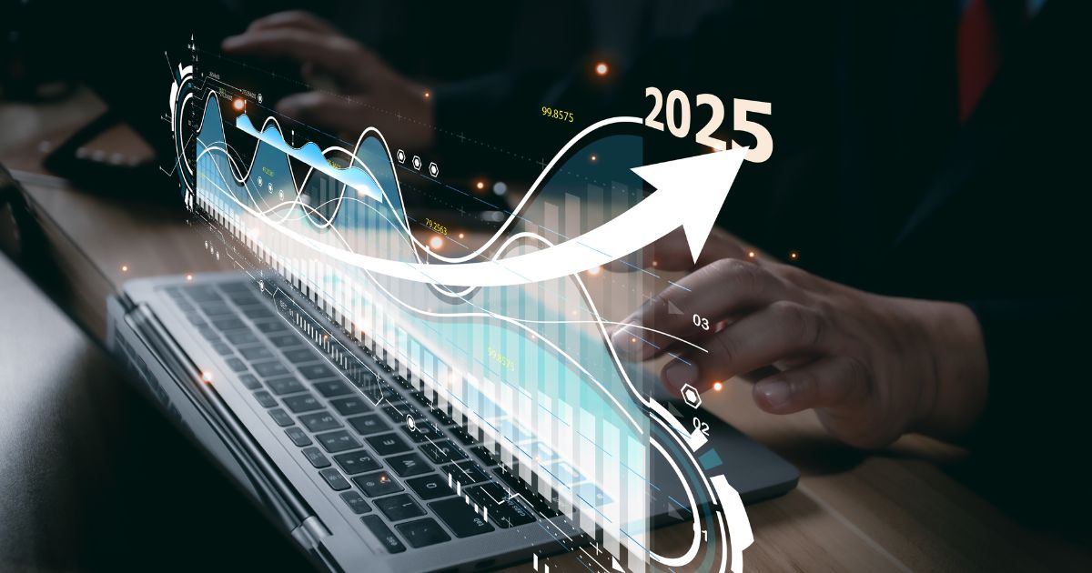 Uma pessoa está digitando em um teclado de laptop, enquanto uma sobreposição gráfica aparece na tela. Essa sobreposição exibe elementos visuais relacionados à análise de dados e projeções de crescimento financeiro, incluindo linhas, gráficos de barras e uma seta apontando para cima. No canto superior direito, destaca-se o ano "2025", e há também valores numéricos visíveis, como "99.8575", sugerindo métricas ou indicadores de desempenho.