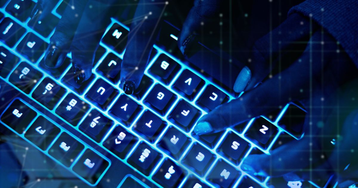 Simulação de cibercrime com imagem em close-up de mãos digitando em um teclado retroiluminado com luz azul. As teclas estão iluminadas e os dedos estão posicionados sobre diferentes teclas. (Anthropic, coding)