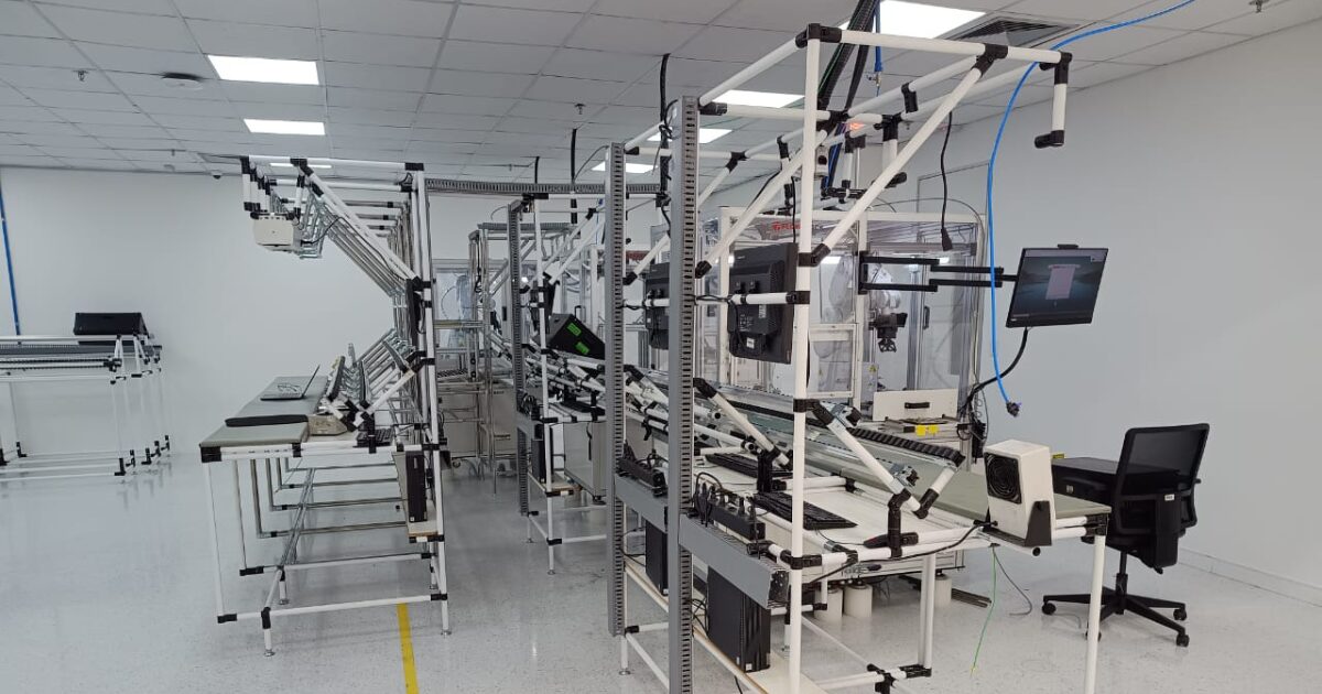 Linha de montagem automatizada em uma fábrica da Lenovo, com esteiras, monitores, estruturas metálicas e equipamentos de alta tecnologia organizados em ambiente limpo e iluminado.