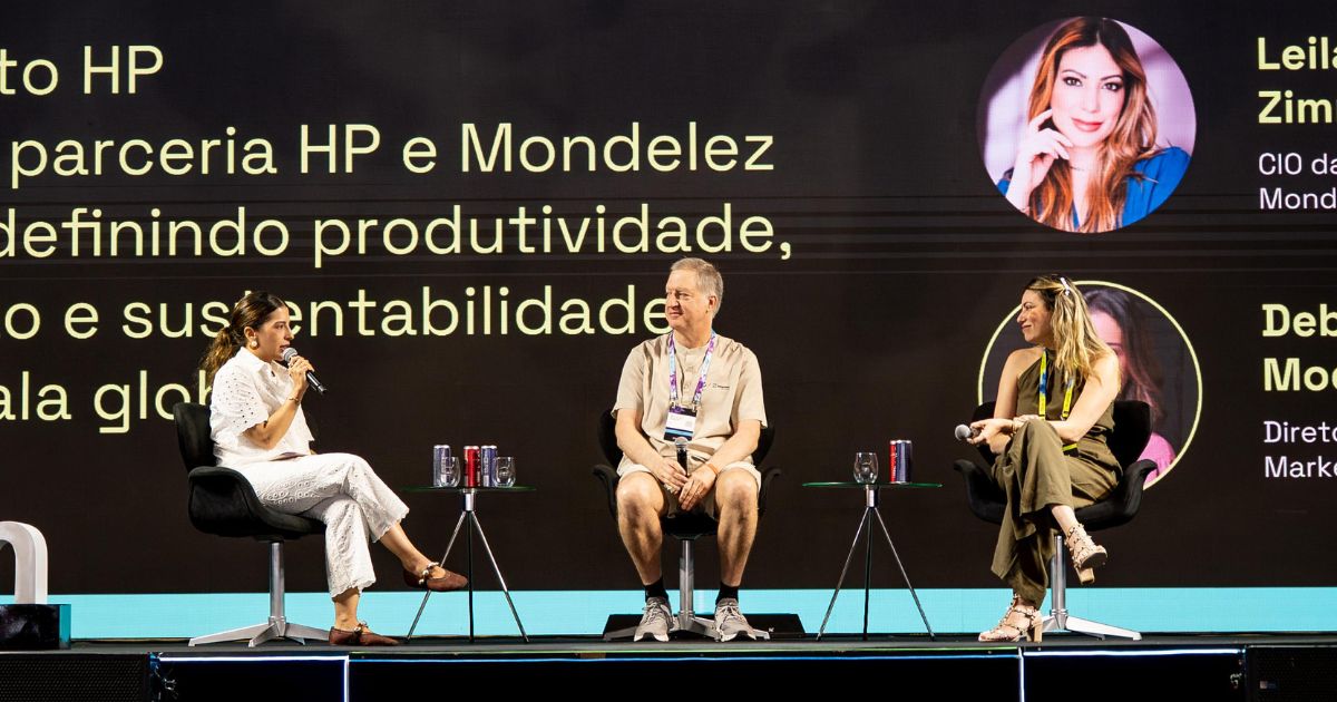 Três pessoas estão sentadas em um palco participando de uma discussão em painel. Ao fundo, um telão exibe o texto: "parceria HP e Mondelez definindo produtividade, e sustentabilidade global". Também aparecem os nomes e cargos de duas participantes: "Leila Zim – CIO da Mondelez" e "Deb Mo – Diretora de Marketing".