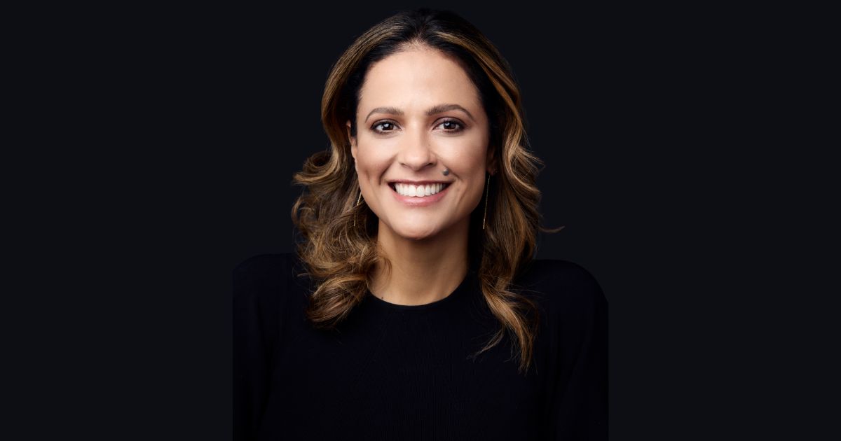 Mulher sorridente em foto de estúdio, com cabelo castanho ondulado e mechas mais claras, vestindo blusa preta. Fundo liso escuro. Trata-se de Alaine Charchat, CIO da Reckitt para a América Latina (Líder)