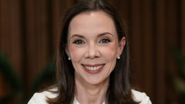 Mulher sorridente em close, de cabelos lisos e castanhos, usando brincos de pérola e roupa clara. A legenda informa que é Cintia Scovine Barcelos, do Bradesco.