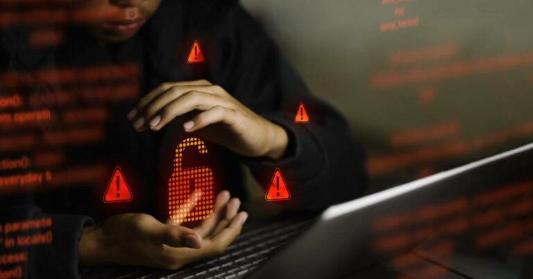 Pessoa parcialmente visível usando laptop no escuro, com as mãos em volta de um ícone digital de cadeado aberto iluminado em vermelho, cercado por símbolos de alerta, representando vazamento de dados ou falha de segurança (paralisa)