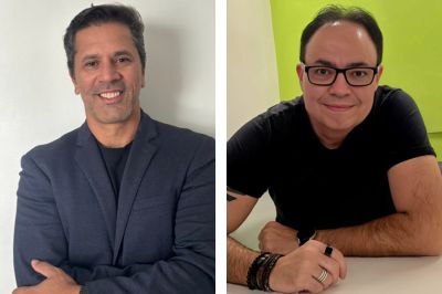 Duas pessoas — uma de blazer escuro e outra com camiseta preta
A primeira veste blazer azul‑escuro e está em frente a um fundo branco.
A segunda está apoiada sobre uma mesa branca, usando camiseta preta e acessórios como pulseiras e anéis. O fundo é verde vivo.