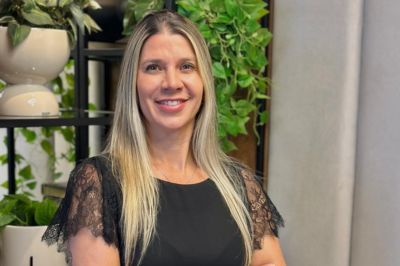 Mulher de blusa preta com mangas de renda Mulher usando uma blusa preta com mangas de renda e calça escura. Ela está em um ambiente interno decorado com muitas plantas em estantes.