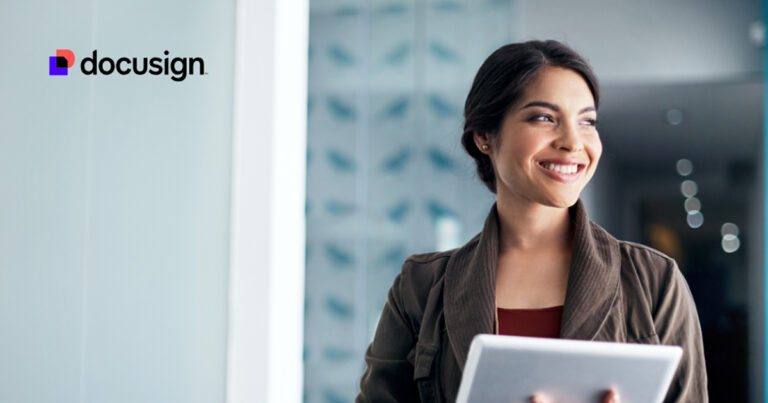 Uma mulher segurando um tablet sorri enquanto está dentro de um ambiente de trabalho; o logotipo da DocuSign IAM aparece no canto superior esquerdo.