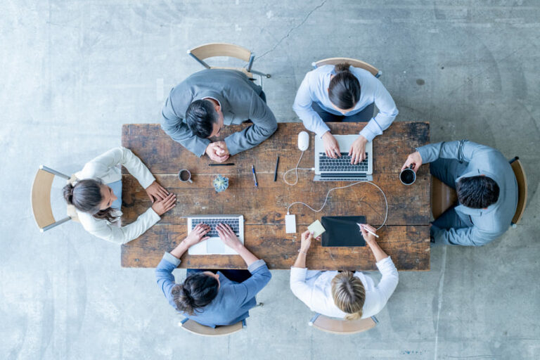Reunião de equipe empresarial discutindo eventos fiscais em uma mesa de escritório, com laptops, tablets e café, promovendo planejamento tributário.