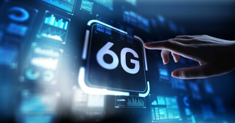 Imagem de uma interface digital futurista em tons de azul, exibindo o texto “6G” no centro de um painel luminoso. À direita, uma mão humana se aproxima da tela com o dedo estendido, como se estivesse prestes a tocar ou ativar o painel. Ao fundo, há diversos gráficos, diagramas e telas flutuantes com dados e visualizações tecnológicas, sugerindo conectividade avançada, redes de comunicação e inovação. O conjunto transmite a ideia de tecnologia de próxima geração e interação homem-máquina.