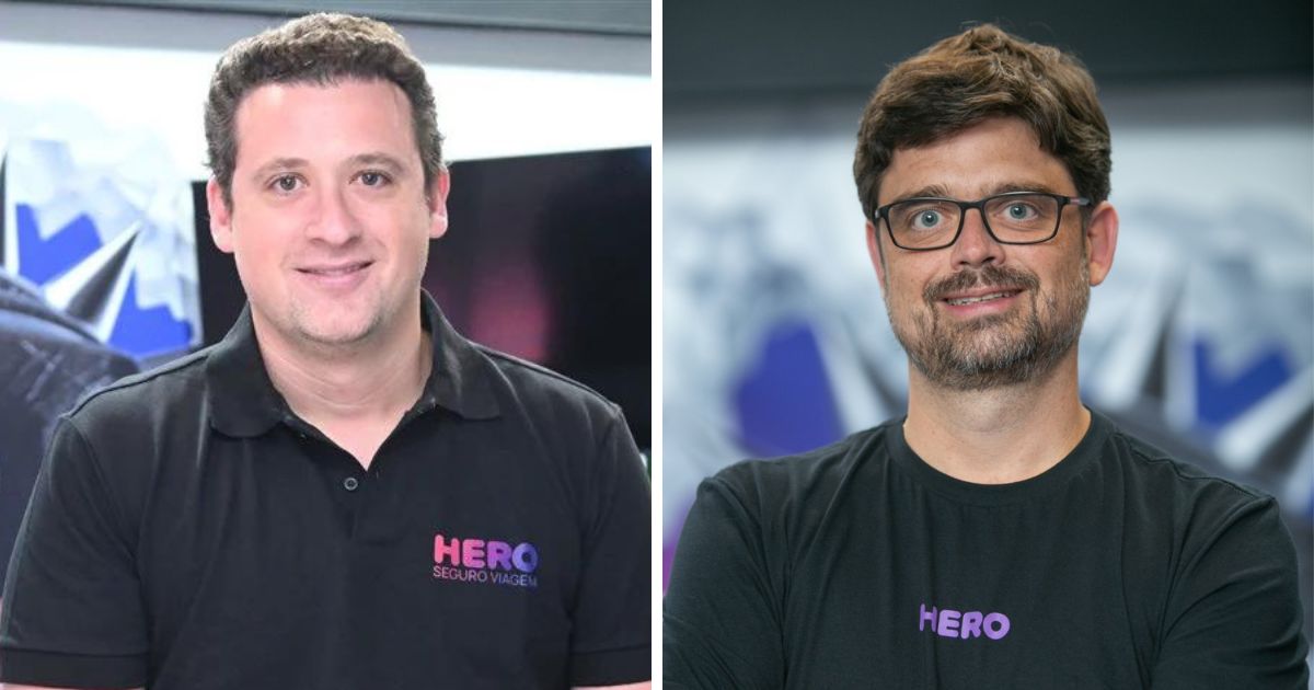Imagem composta por dois retratos colocados lado a lado. À esquerda, uma pessoa posicionada de frente para a câmera, vestindo camisa polo preta com o logotipo “HERO Seguro Viagem” em cores roxa e rosa. O enquadramento mostra o tronco e o rosto, com expressão neutra e fundo interno desfocado com elementos gráficos. À direita, outra pessoa também de frente para a câmera, vestindo camiseta preta com o logotipo “HERO” em roxo. Essa pessoa usa óculos, tem barba curta e cabelos curtos. O fundo é semelhante ao da primeira imagem, interno e desfocado, sugerindo o mesmo ambiente corporativo. A iluminação é uniforme em ambos os retratos. (Hero Seguros)